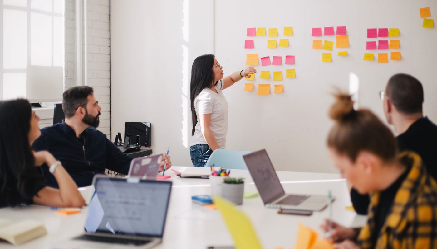 Marketing Manager header image of a woman presenting to a team with a range of post-it notes on the wall