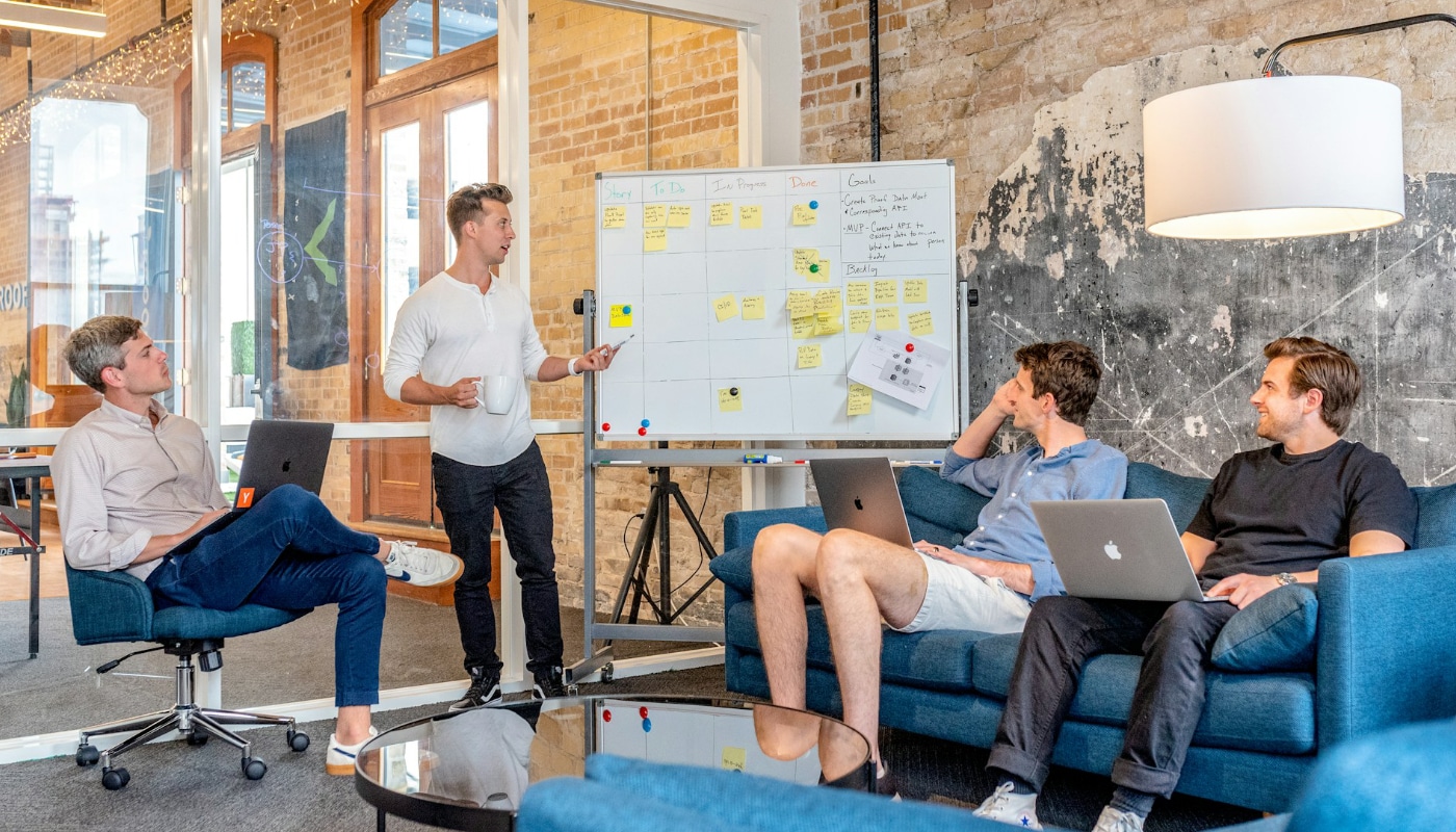 Multi-Channel Marketer header image of four men looking at a whiteboard covered in post it notes while they use laptops