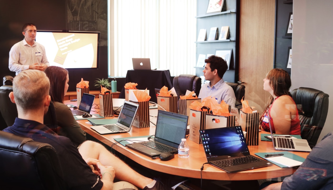 Business Administrator header image of a boardroom table with one man presenting to four other people, all using laptops