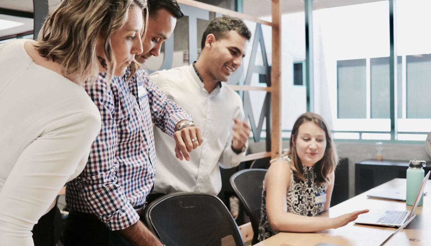 Management Apprenticeships header image of four people at a desk having a discussion about something on a laptop